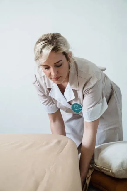 Une femme de ménage professionnelle en combinaison rouge passe l’aspirateur dans un salon moderne avec un aspirateur jaune.
