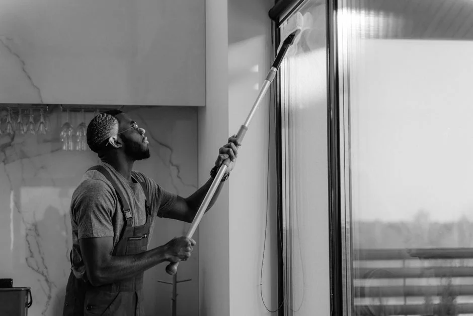 Une professionnelle du nettoyage, vêtue d’une combinaison rouge, passe l’aspirateur dans un salon moderne à l’aide d’un aspirateur jaune.